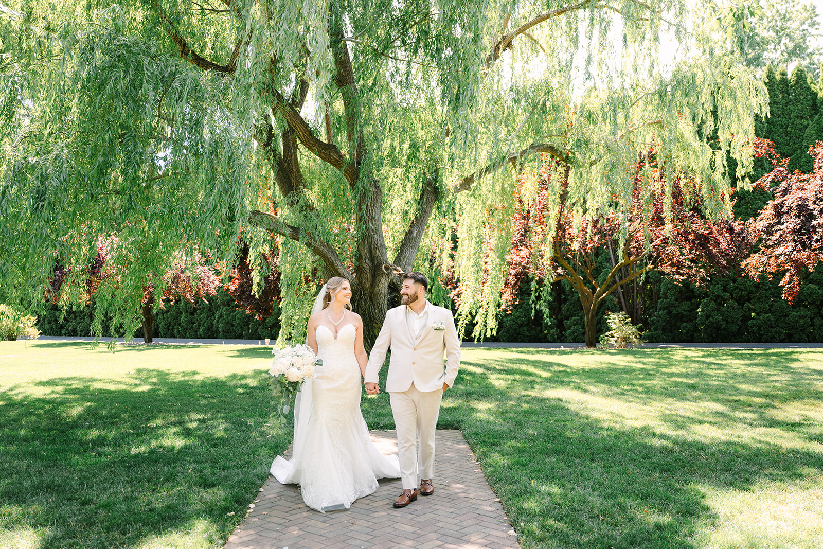 bride and groom walking with a weeping willow behind them