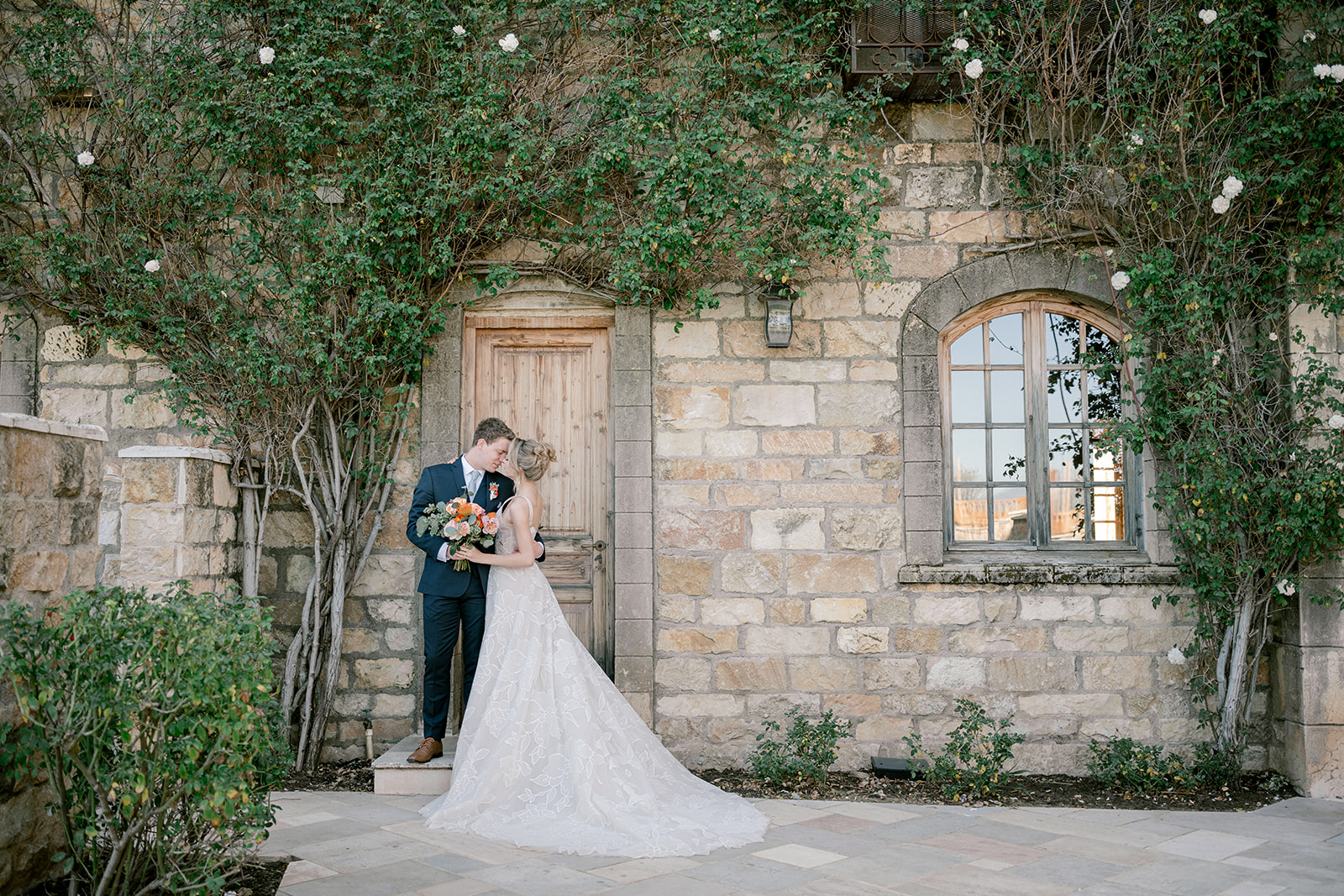 bride in groom standing in front a stone building with climbing vines