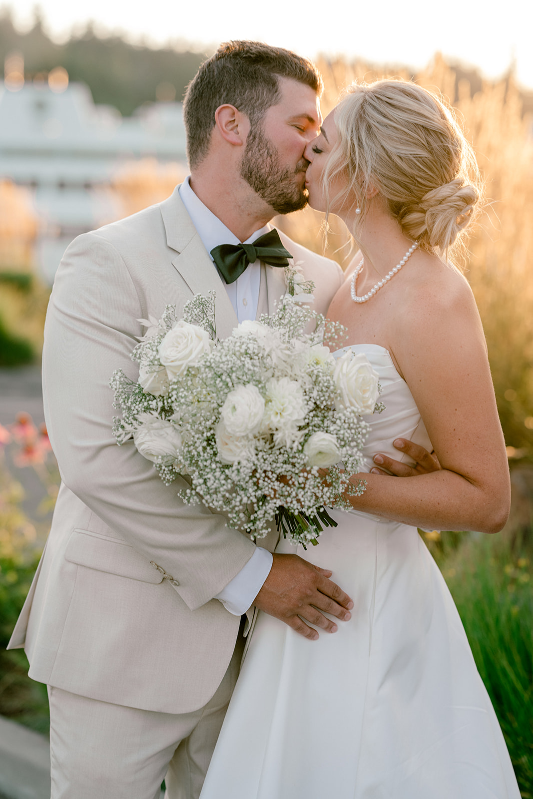 Groom in tan suit kissing bride in the golden light